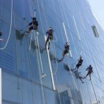 Multiple workers rope-cleaning a glass skyscraper facade